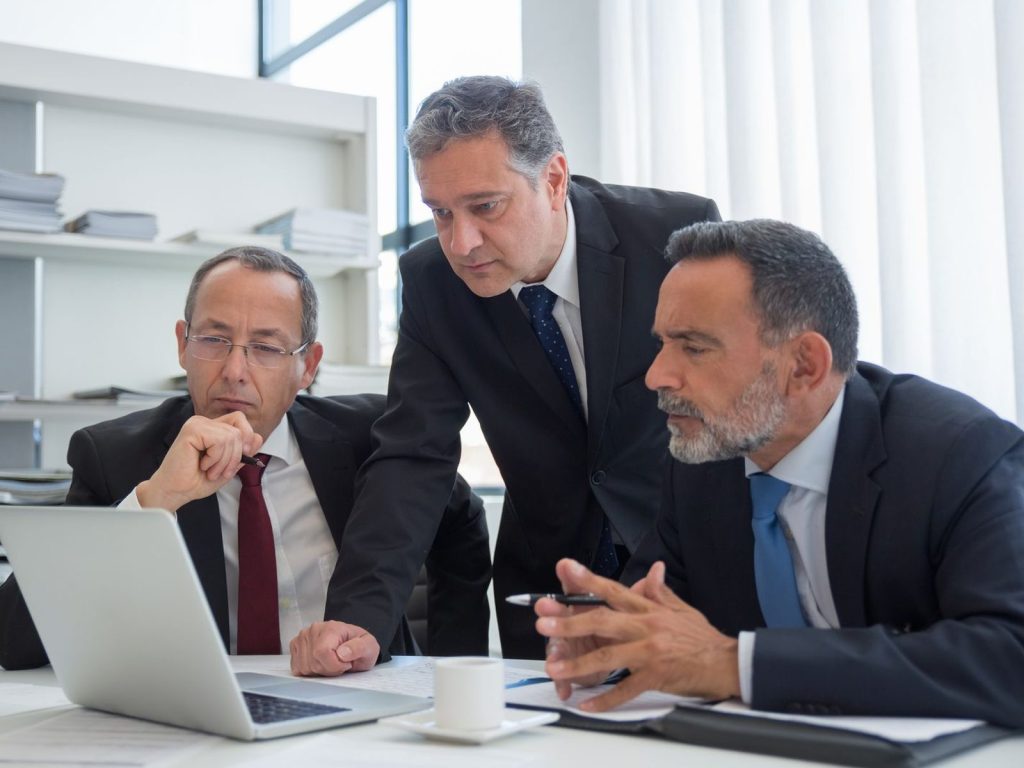 Executives in suits reviewing work together on a laptop