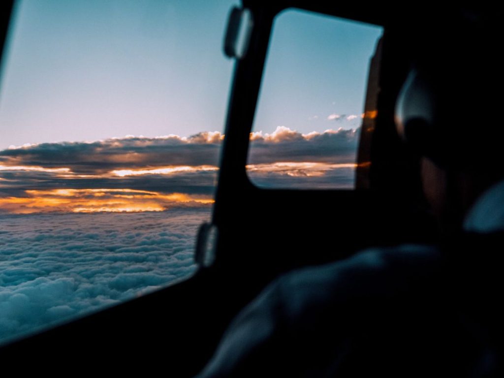 Pilot in a darkened cockpit above the clouds at sunset