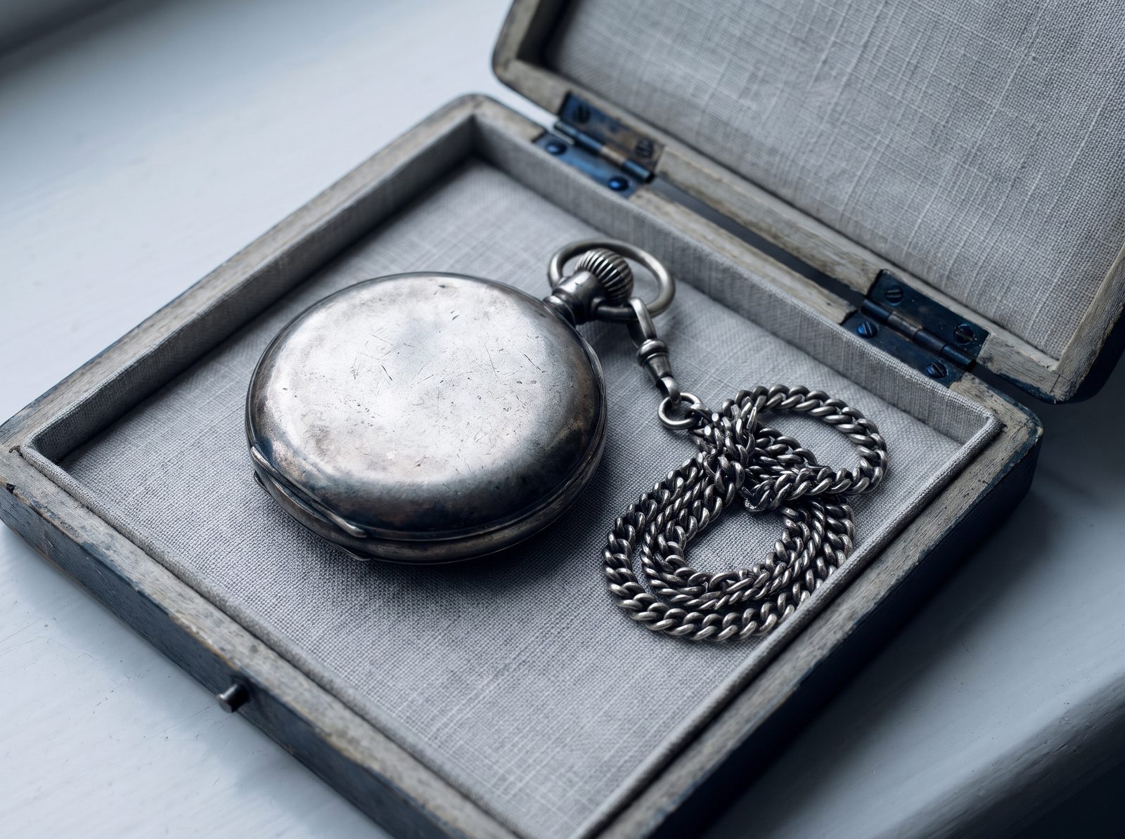 A silver pocket watch and chain resting in its open presentation box.