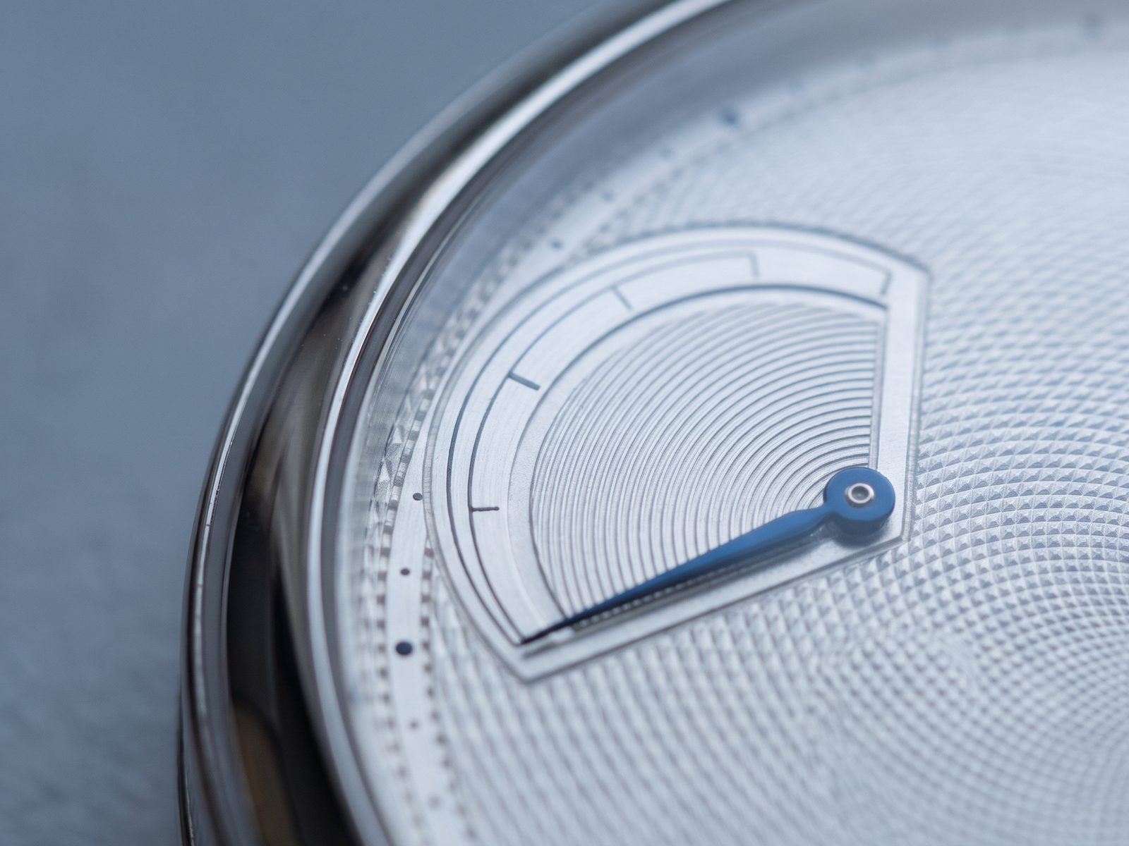 Macro photograph of a silver watch dial with a blued-steel power reserve hand.