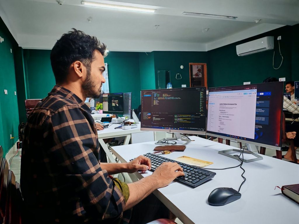 Software developer coding at a dual monitor setup in an office